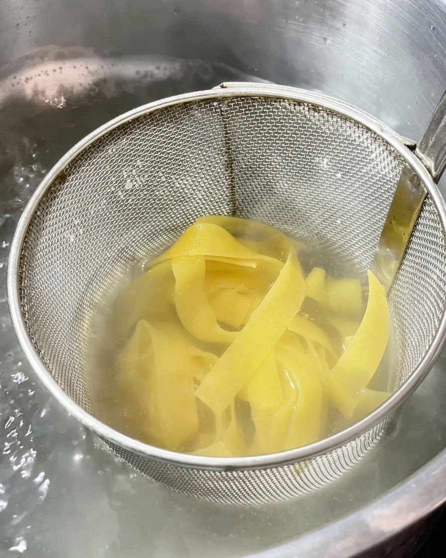 Pasta lunga a nastro che cuoce in un cestello di metallo immerso in una pentola dacqua bollente.