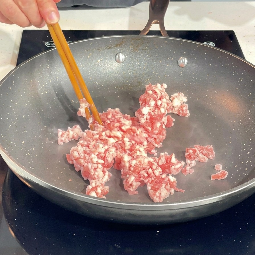 Utilizzo di bacchette per sgranare la carne macinata di maiale cruda in una padella calda.