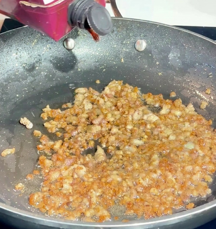 Vino rosso versato da un piccolo brick in una padella con carne di maiale rosolata.