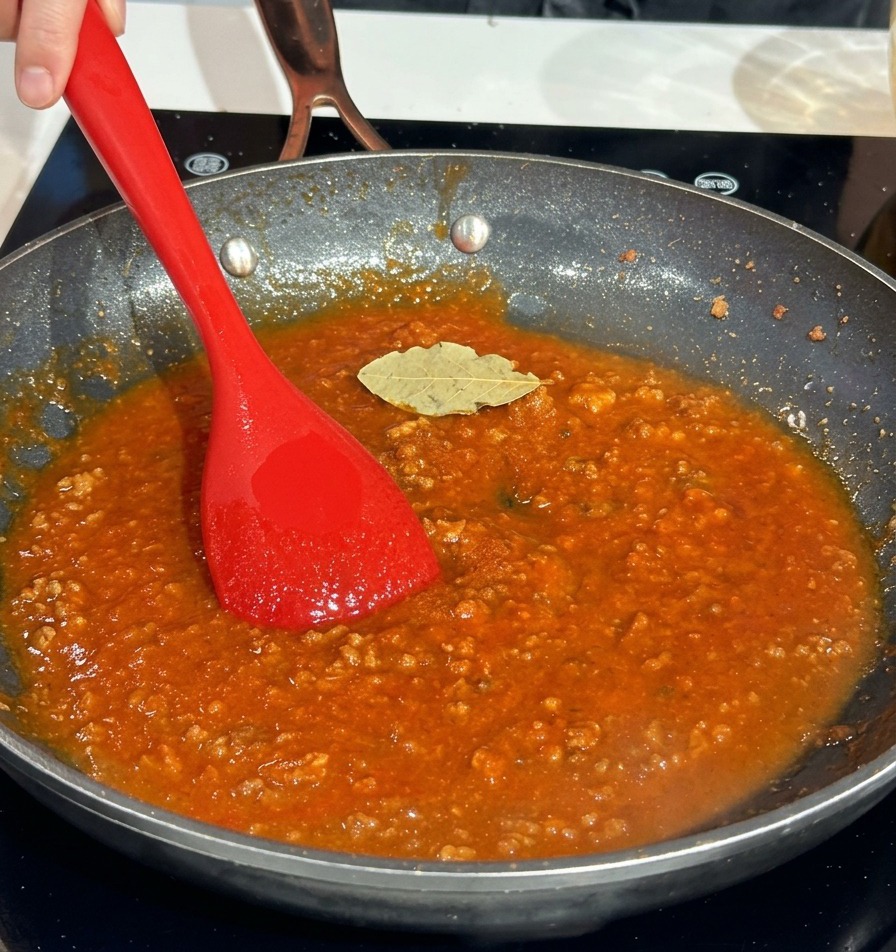 Una foglia di alloro appoggiata sopra un ricco ragù di carne rosso in padella.
