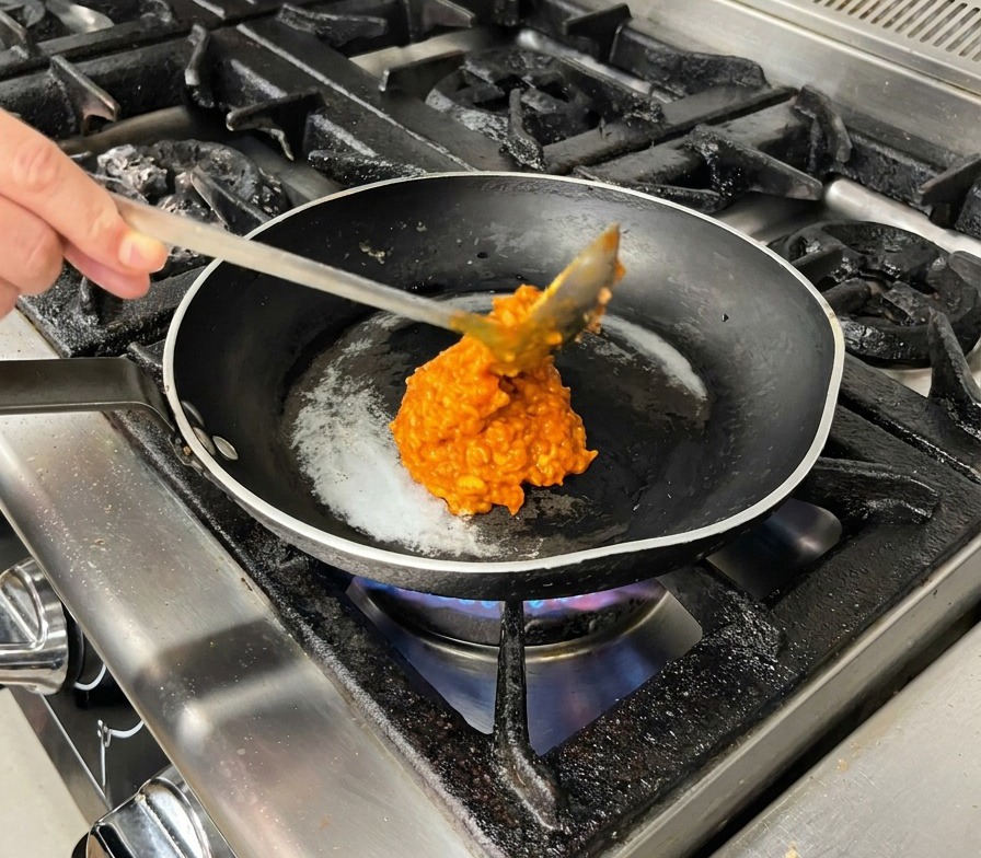 Un cucchiaio di ragù di carne denso e rosso viene messo in una padella nera calda.