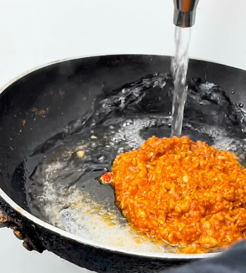 Un getto dacqua viene versato in una padella nera con del ragù rosso che sobbolle.