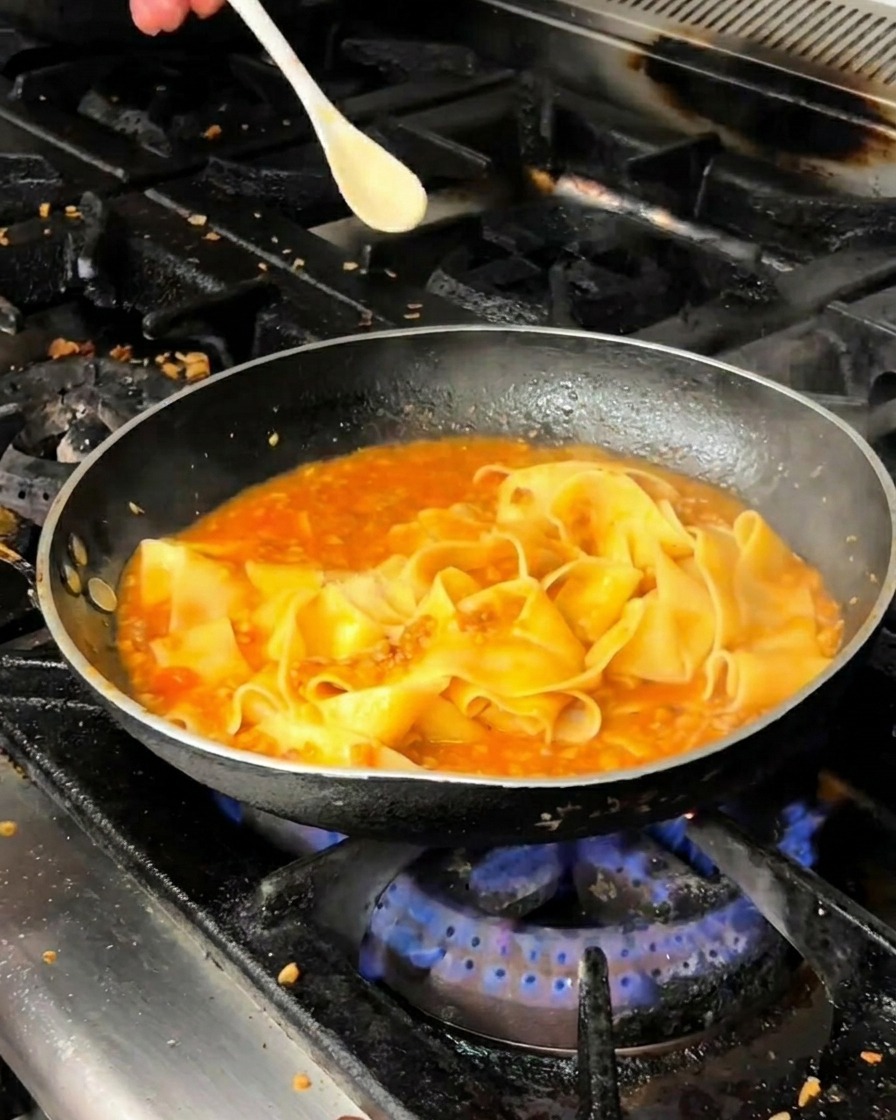 Pappardelle in padella con ragù rosso sul fuoco.