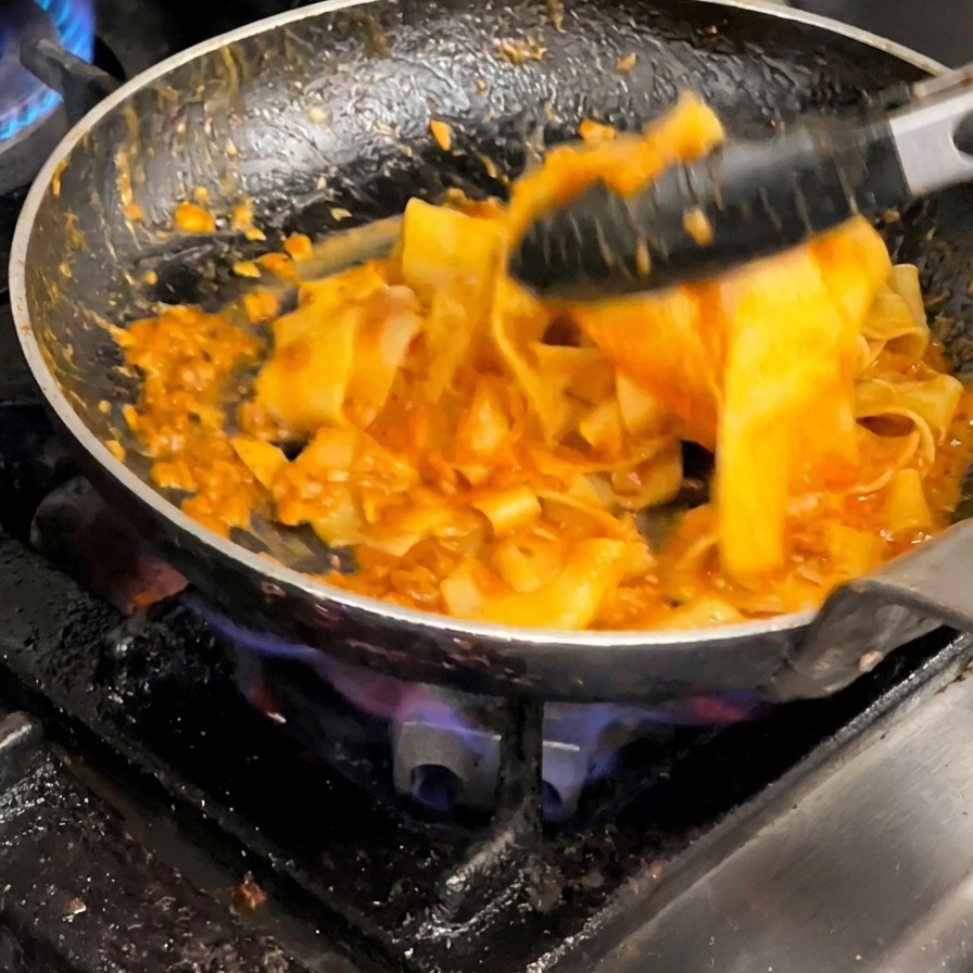 Uso di pinze per saltare le pappardelle con il ragù in padella.