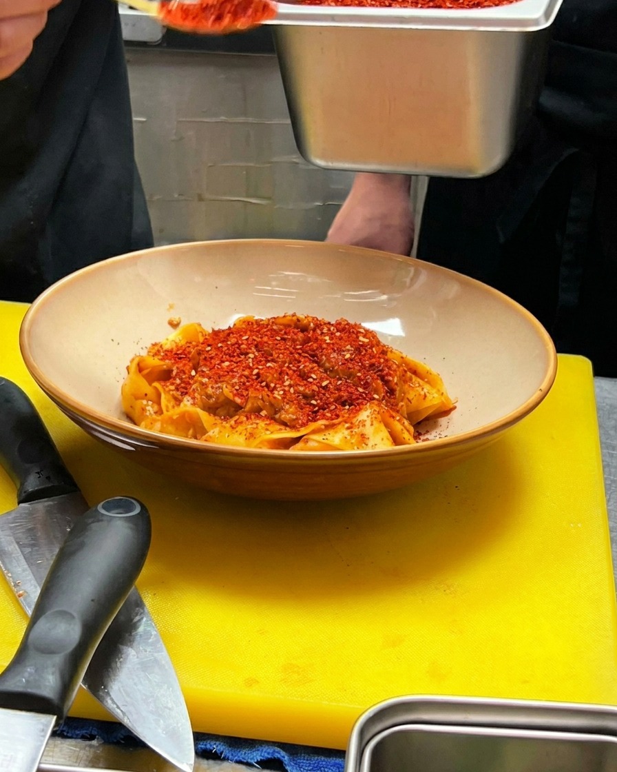 Un cucchiaio di peperoncino rosso in polvere viene versato al centro della pasta impiattata.