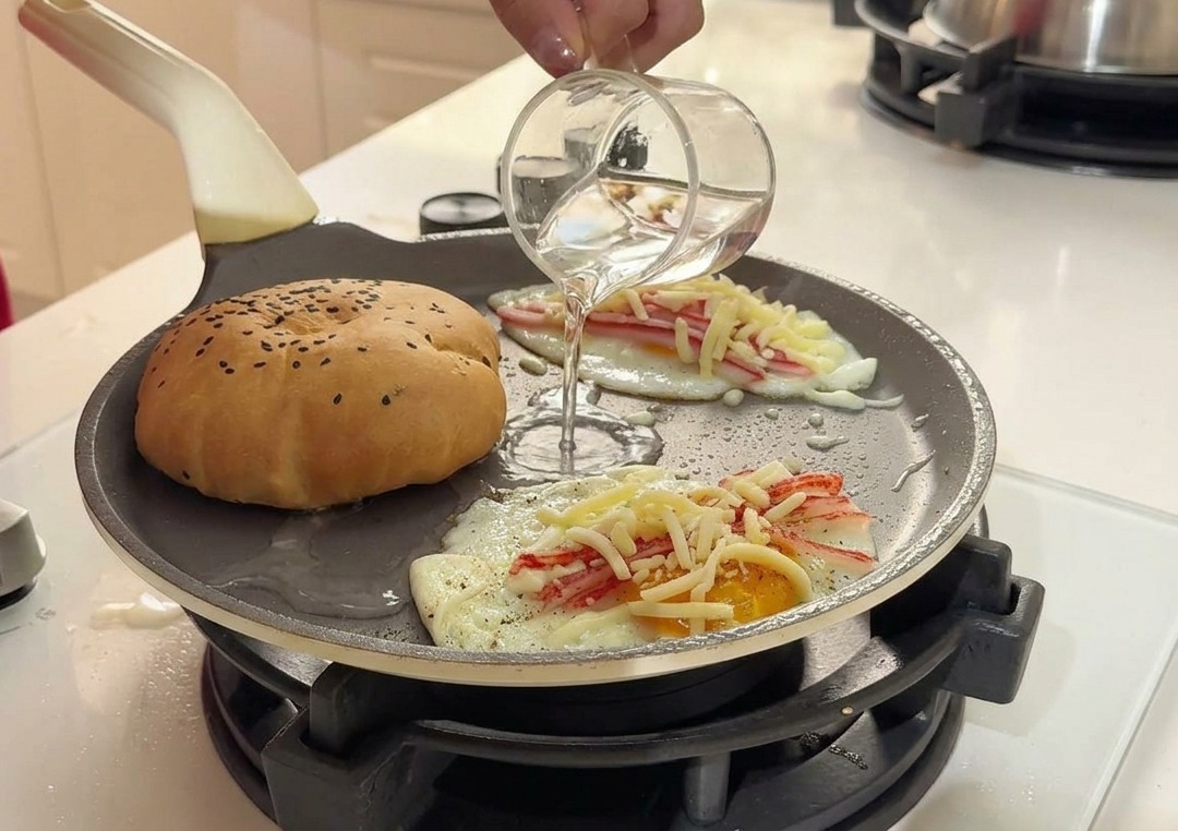 Versamento di acqua limpida da un bicchierino nella padella calda tra il pane e le uova.