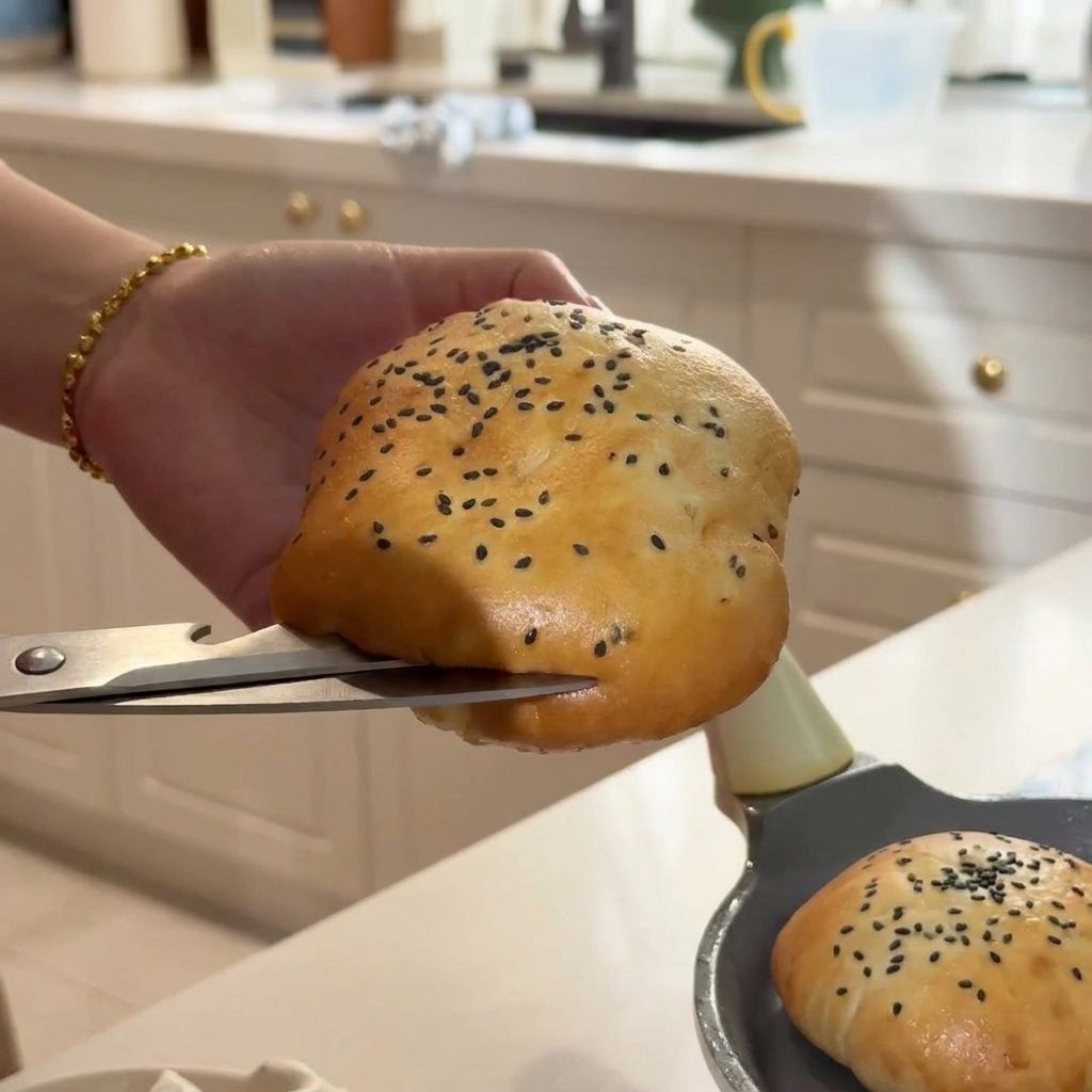 Una mano che taglia con cura un panino caldo al sesamo usando un paio di forbici da cucina argentate.