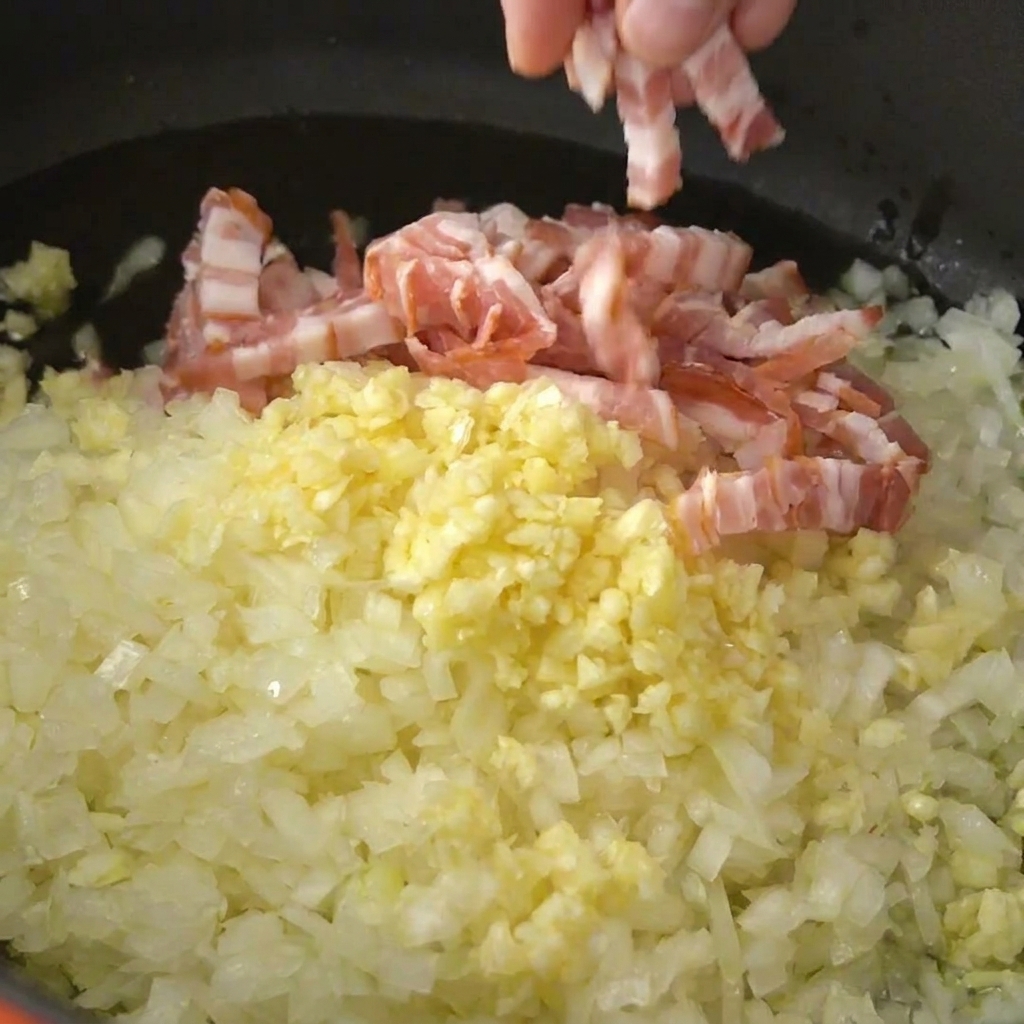 Striscioline di pancetta cruda aggiunte al soffritto di cipolla e aglio in pentola.