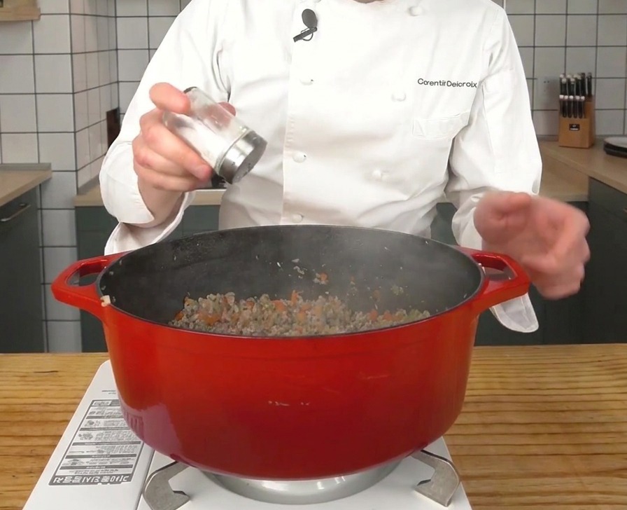 Sale che viene sparso sulla carne rosolata allinterno di una grande pentola rossa.