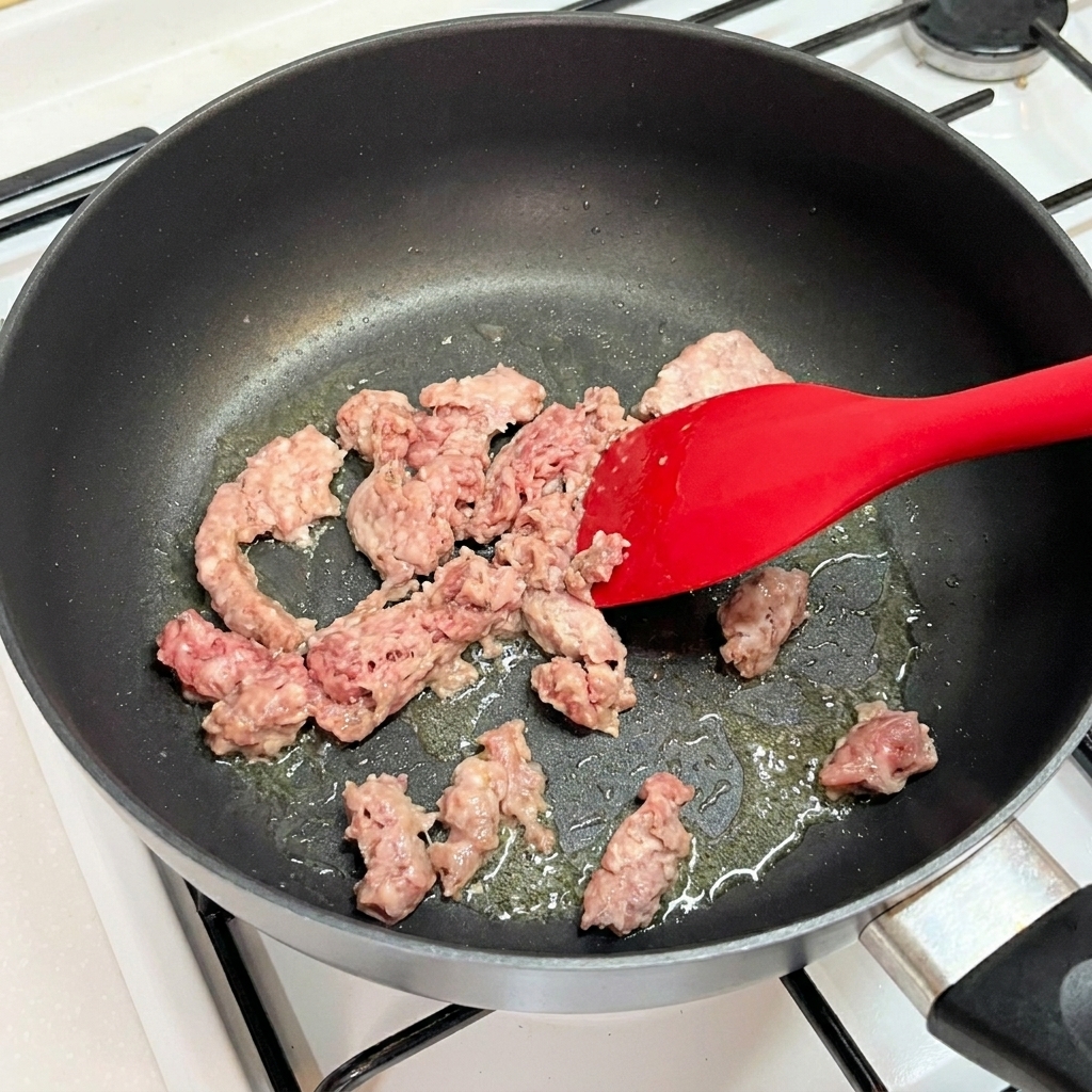 Carne macinata di manzo sgranata in una padella calda con una spatola.