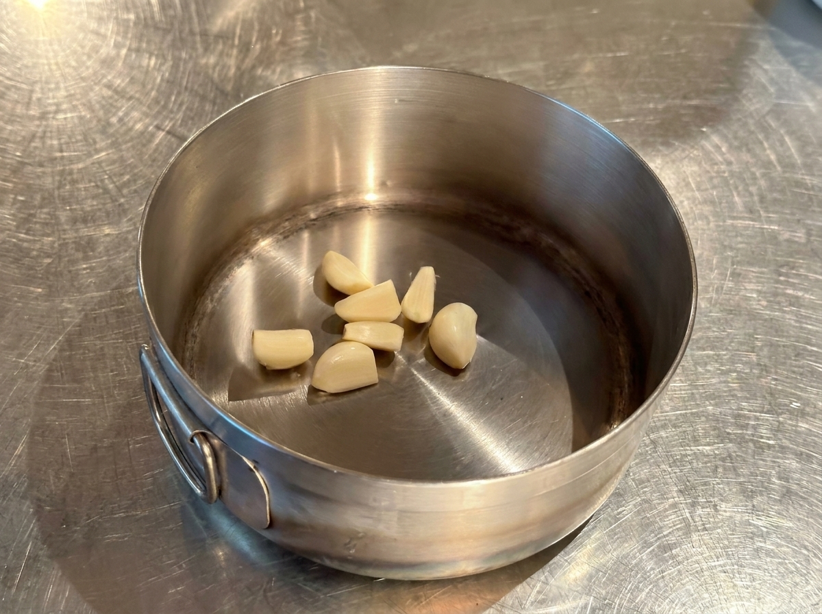 Spicchi daglio interi e pelati sul fondo di un piccolo pentolino in acciaio inossidabile.