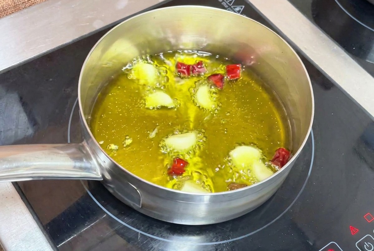 Aglio e peperoncino che soffriggono dolcemente in olio bollente in un pentolino su un fornello a induzione.