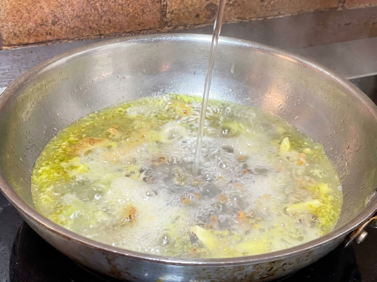 Mestolo di acqua della pasta amidacea versato nella padella con olio e aglio.
