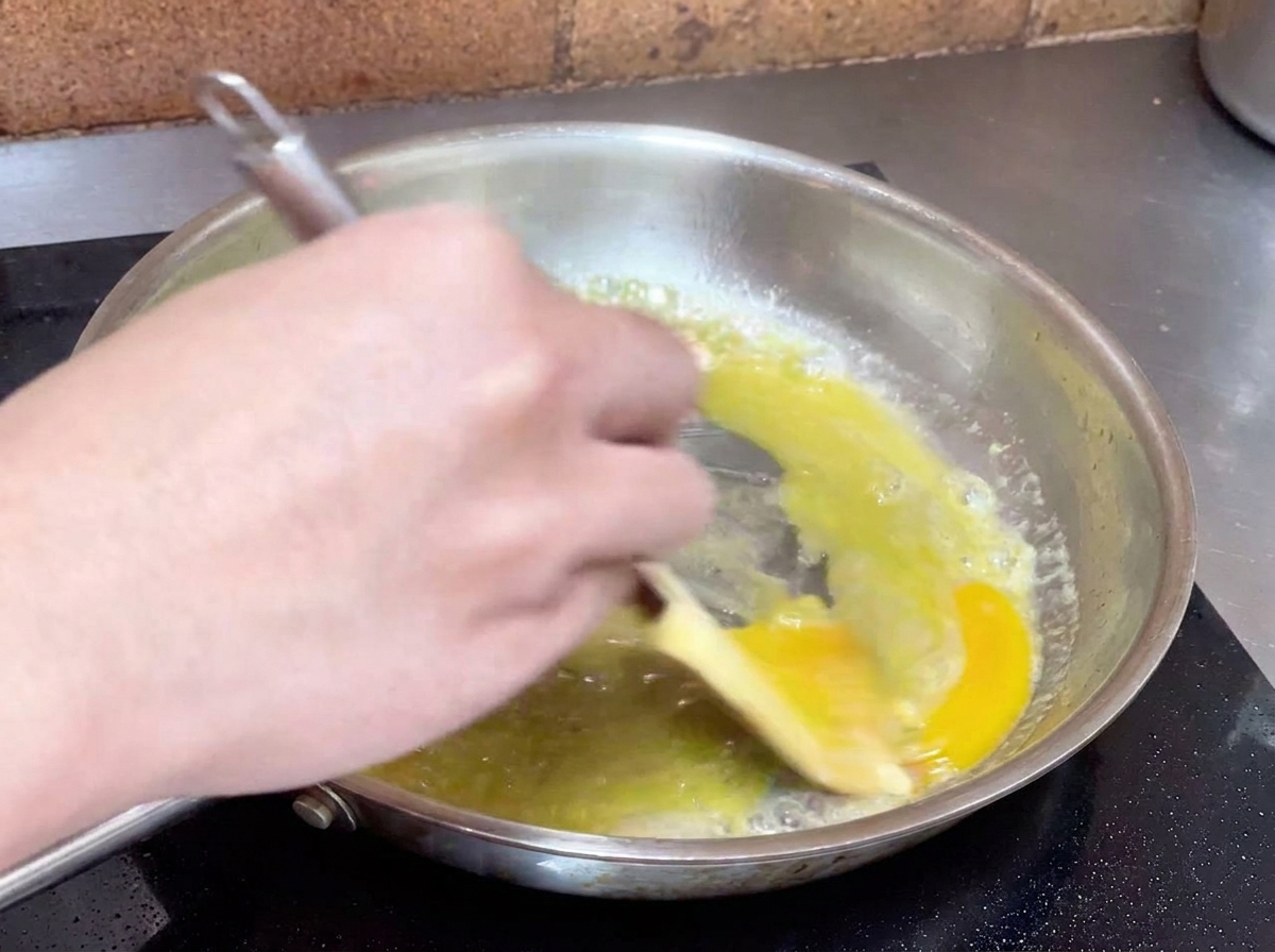Mano che mescola energicamente acqua e olio con una spatola per creare unemulsione cremosa.