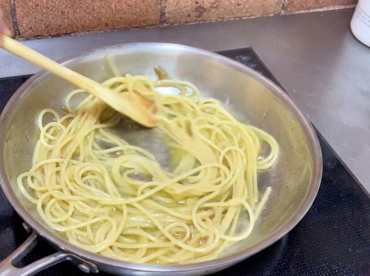 Spaghetti saltati in padella con un cucchiaio di legno per avvolgere la pasta nella salsa allaglio.