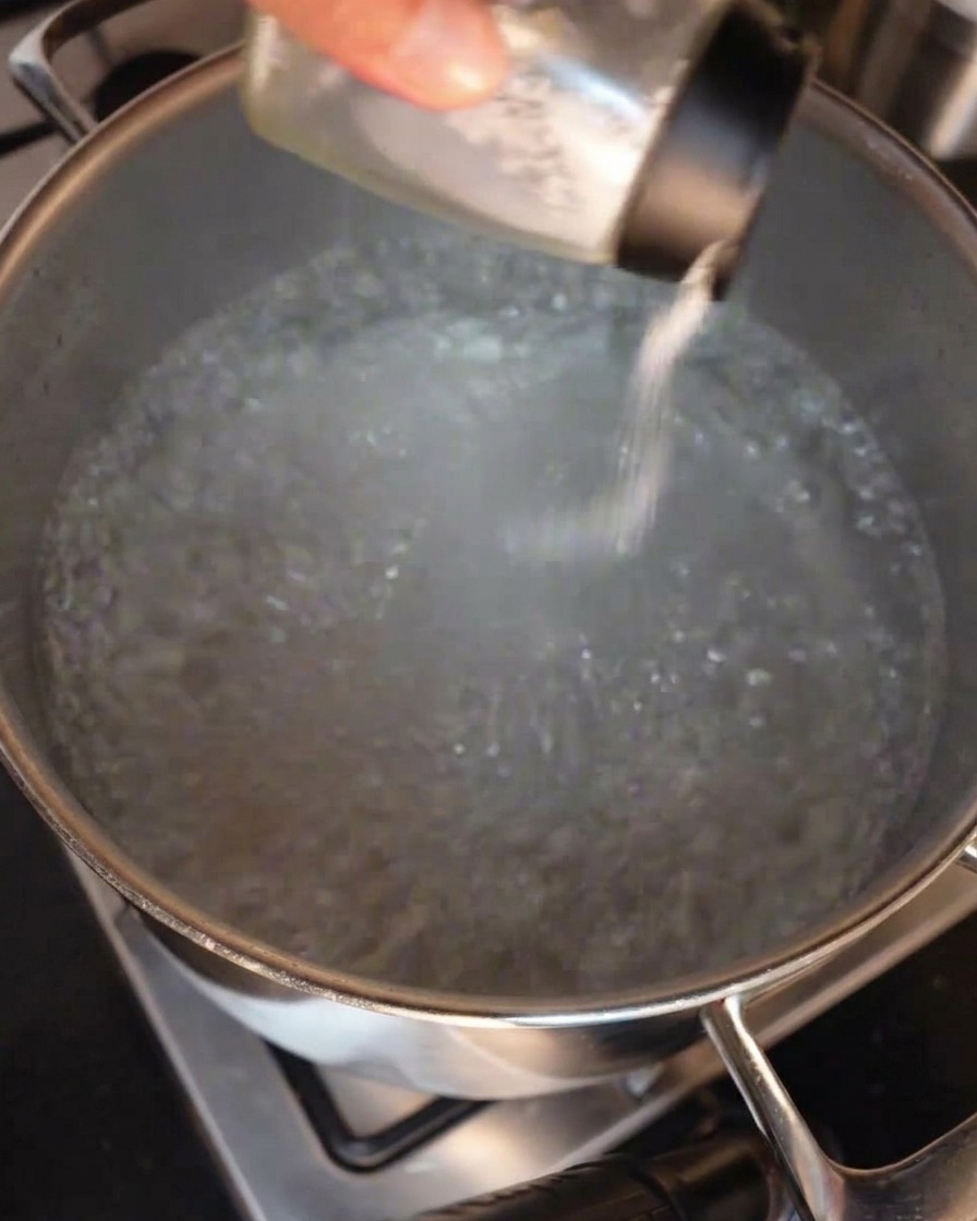 Una mano che versa del sale grosso in una pentola dacqua in ebollizione.