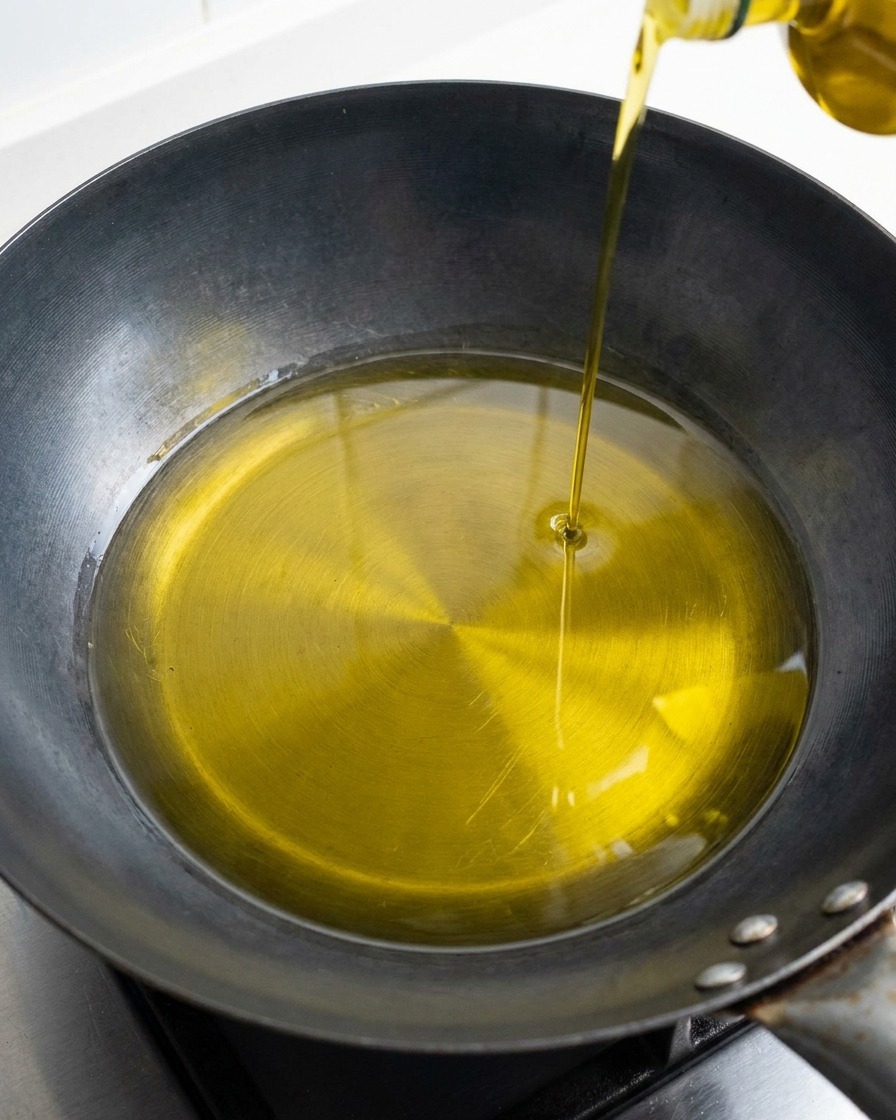 Un flusso dorato di olio doliva versato in una padella o wok dal fondo scuro.