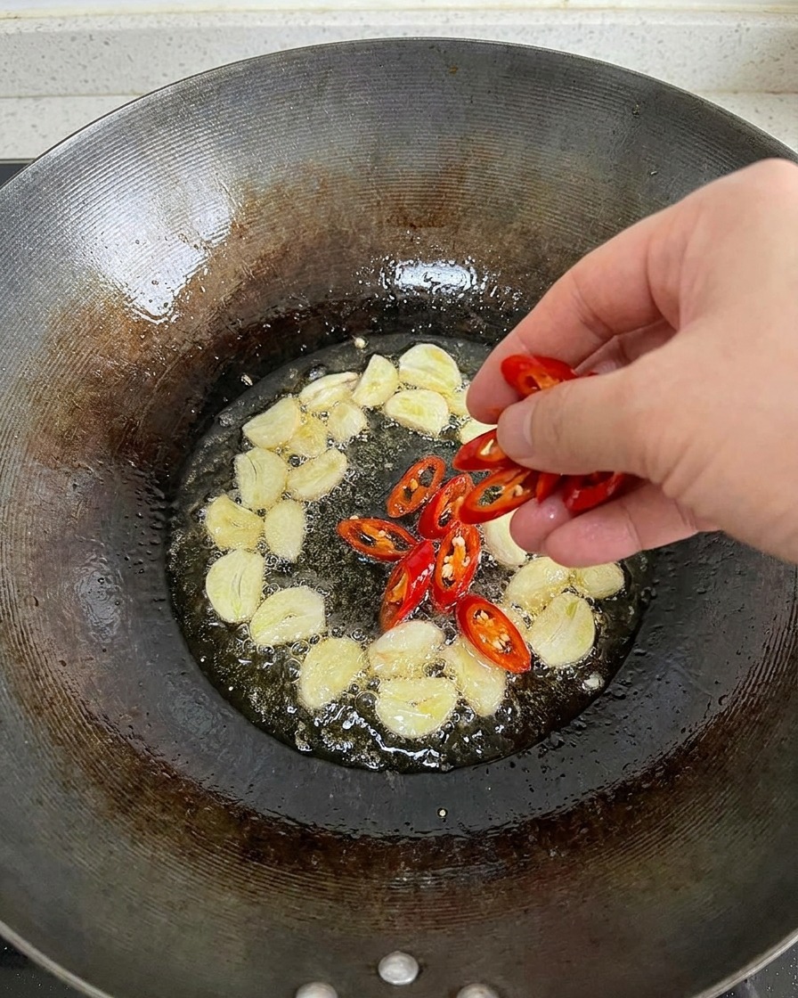 Peperoncini rossi freschi affettati appena tuffati in un wok con olio caldo e fette daglio.