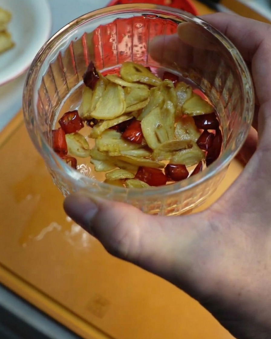 Una piccola ciotola di vetro con allinterno fettine di aglio fritto e peperoncino.