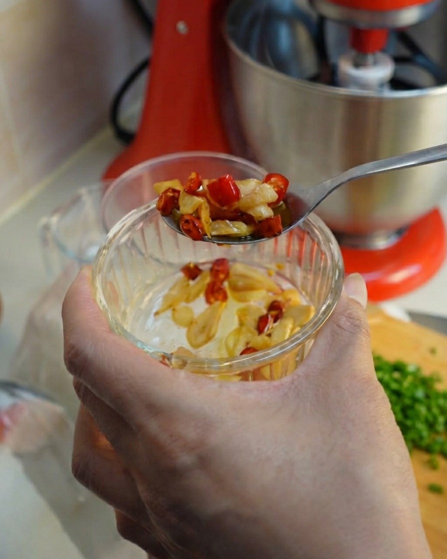 Un cucchiaio che preleva aglio fritto e peperoncino da una ciotolina di vetro.