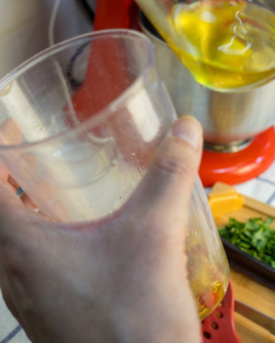 Un frullatore a immersione sollevato da un bicchiere, da cui cola una salsa liscia di colore rosso-dorato.
