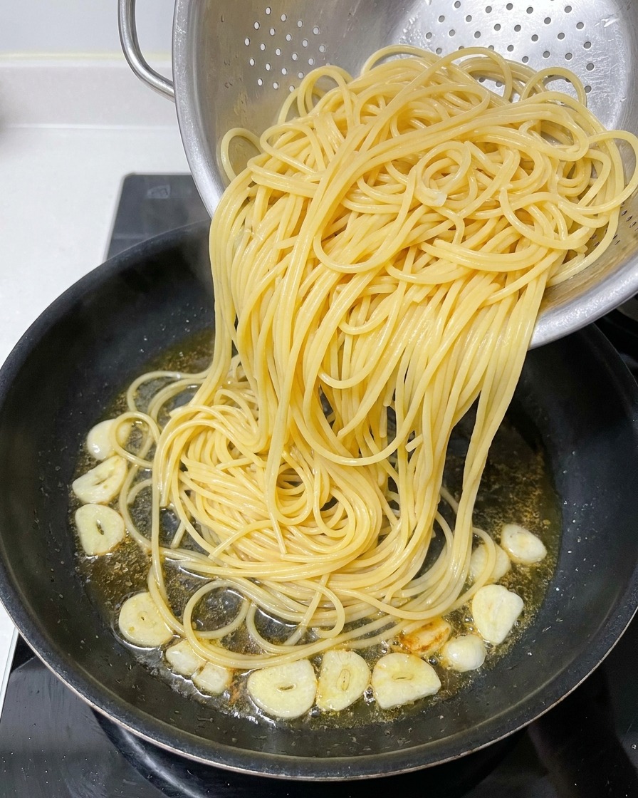 Spaghetti cotti appena trasferiti da uno scolapasta in una padella con olio aromatizzato e aglio.