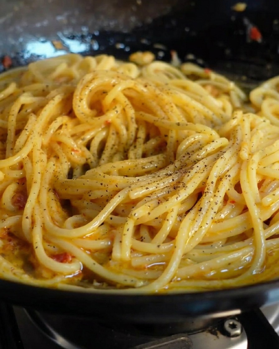 Pepe nero macinato fresco spolverato su una padella di spaghetti lucidi.