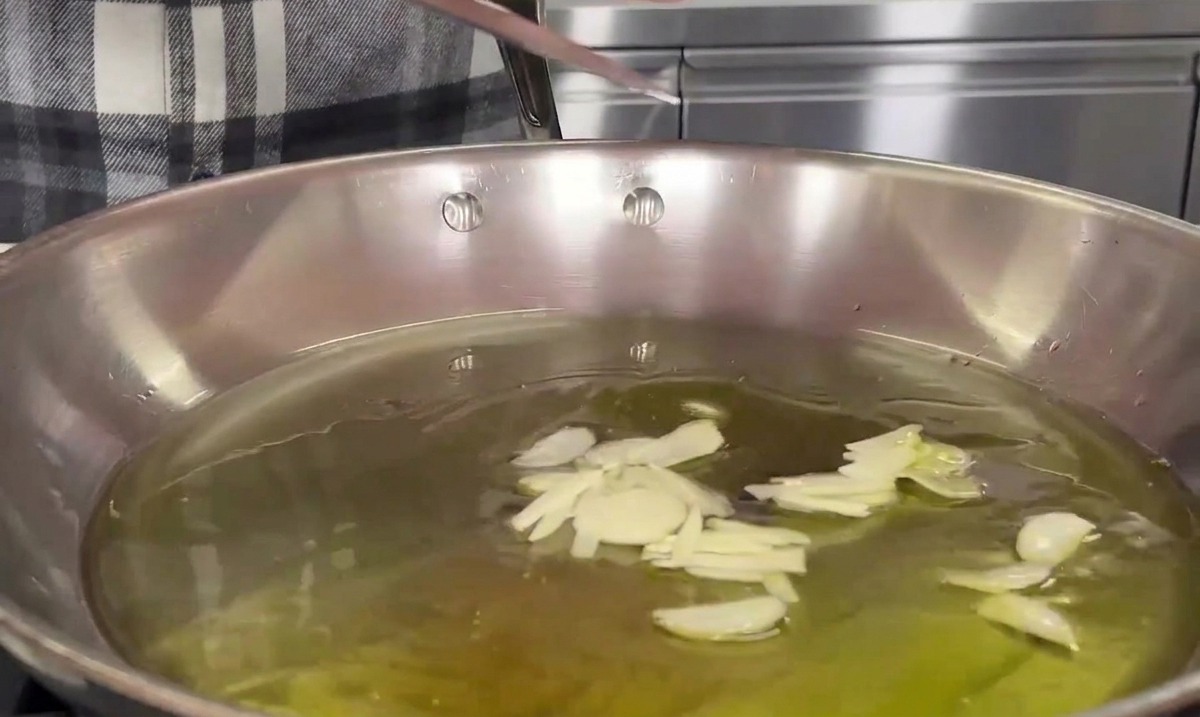 Lama di un coltello che fa scivolare laglio affettato in una padella di acciaio con olio doliva tiepido.