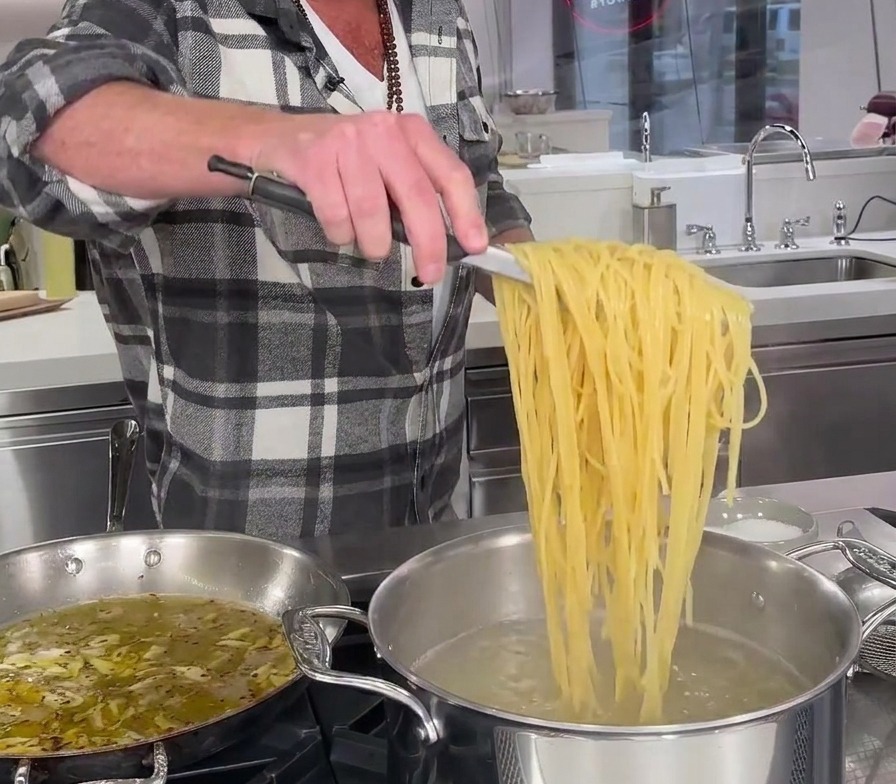 Spaghetti parzialmente cotti sollevati direttamente dalla pentola con acqua bollente usando delle pinze da cucina.
