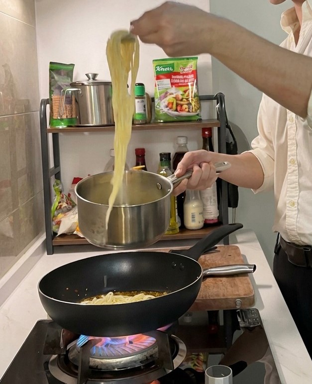 Lunghi fili di spaghetti cotti sollevati da una pentola dacciaio con una pinza, pronti per essere aggiunti a una padella calda con olio condito.