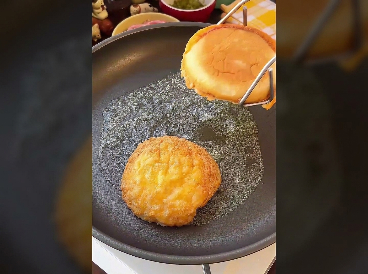 Le due metà di un panino per burger che tostano rivolte verso il basso in una padella imburrata.