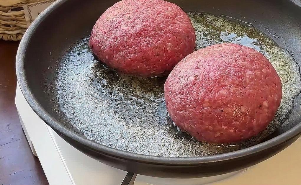 Due spesse polpette di manzo crudo che friggono nel burro fuso su un fornello portatile.
