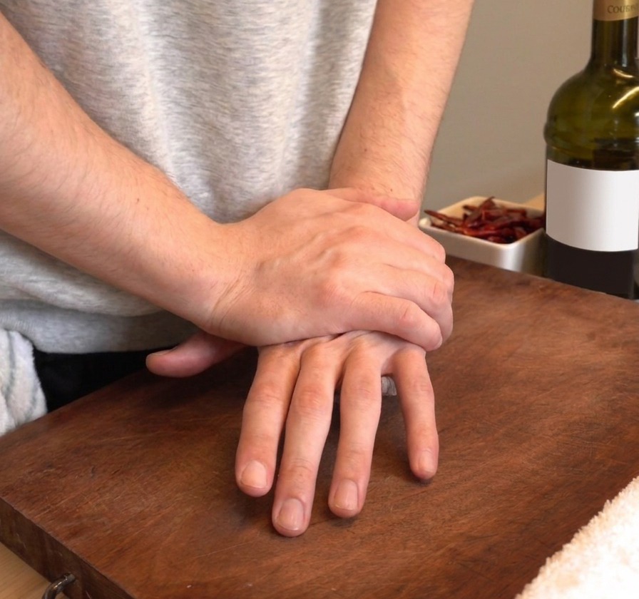 Mani che schiacciano con decisione degli spicchi daglio fresco su un tagliere di legno.
