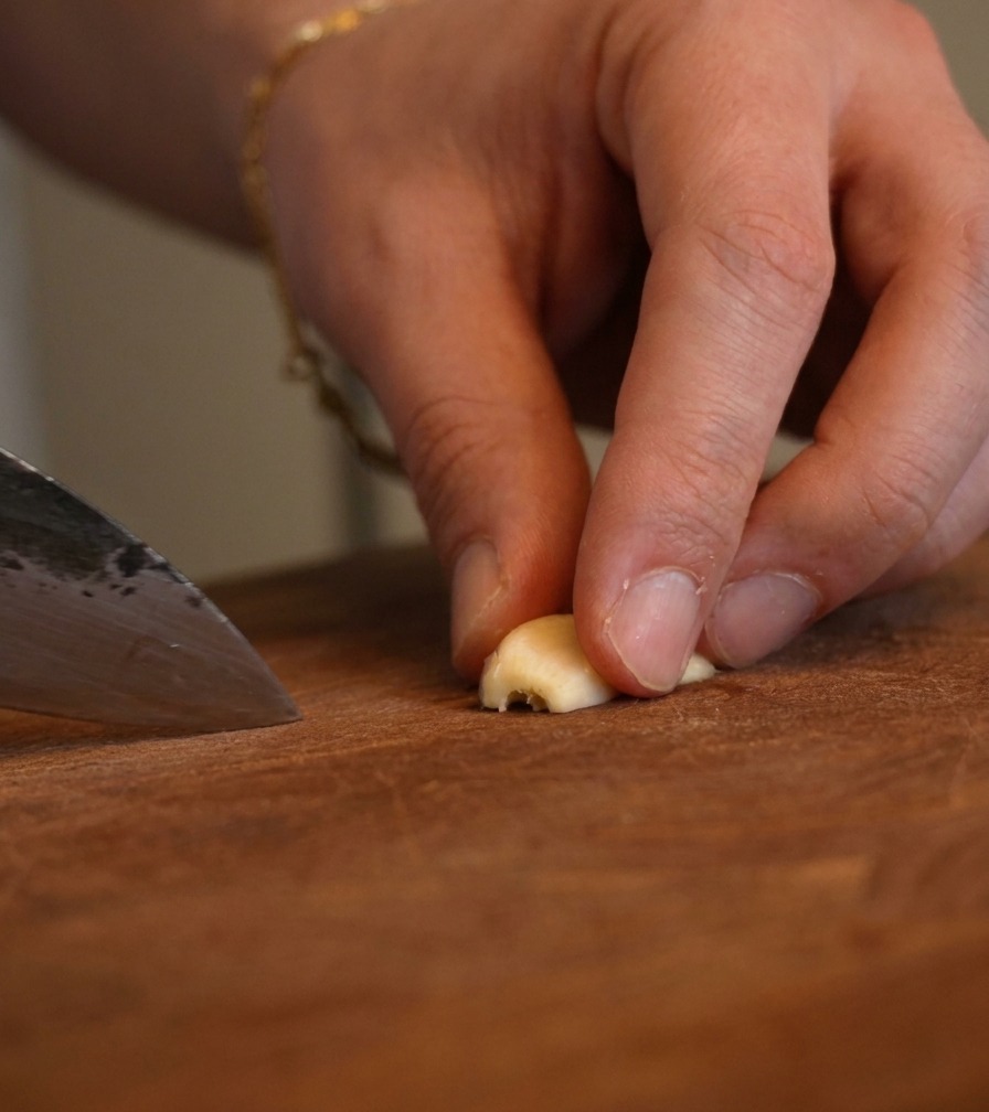 Primo piano di dita che tengono un pezzetto daglio mentre un coltello da chef lo trita finemente.