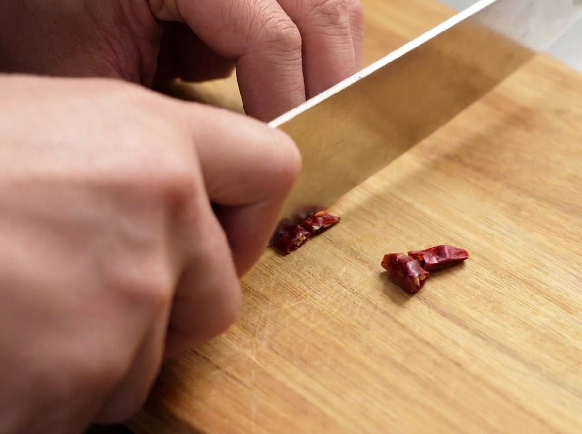 Un coltello che taglia i peperoncini rossi secchi a piccoli pezzi su un tagliere.