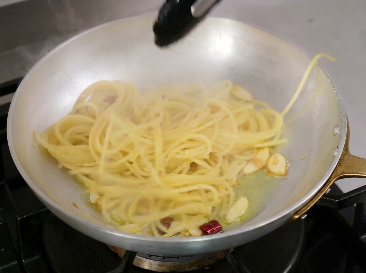 Spaghetti cotti sollevati con pinze da cucina e messi nella padella con lolio aromatizzato.