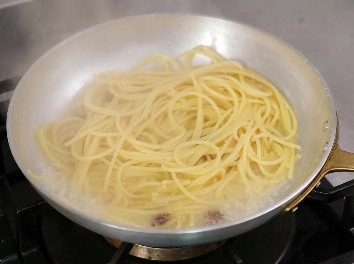 Spaghetti che saltano in padella con acqua di cottura amidacea e olio bollente.