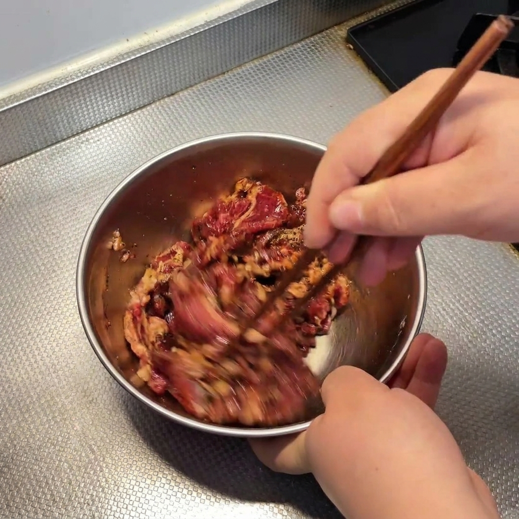 Bacchette di legno che mescolano velocemente il manzo crudo in una ciotola.