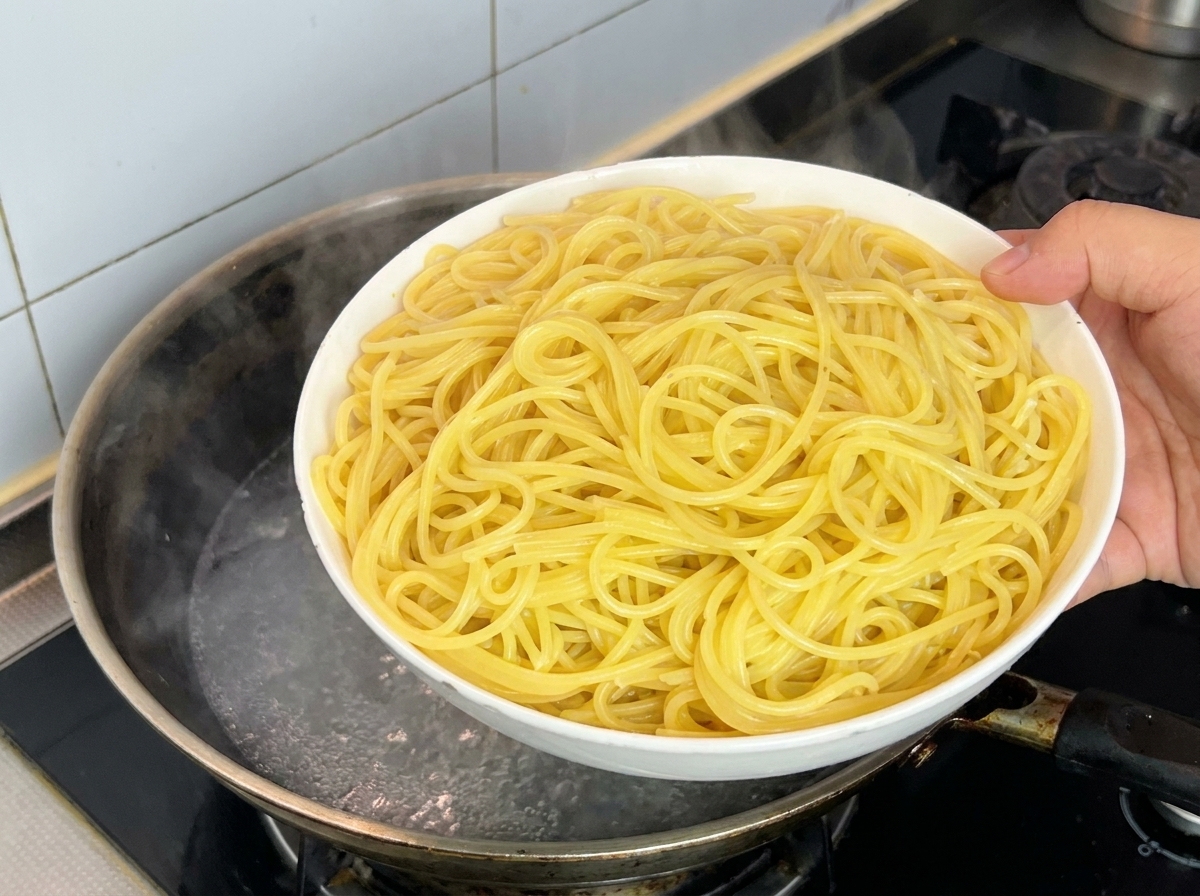 Mano con una ciotola di spaghetti appena bolliti sopra una pentola fumante.