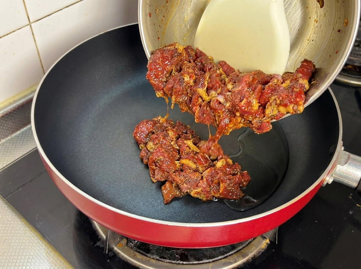 Manzo marinato versato in una padella rovente con olio.