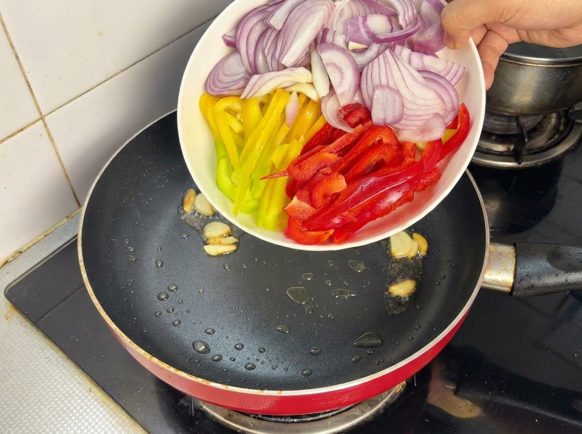 Cipolle e peperoni a listarelle aggiunti in una padella calda.