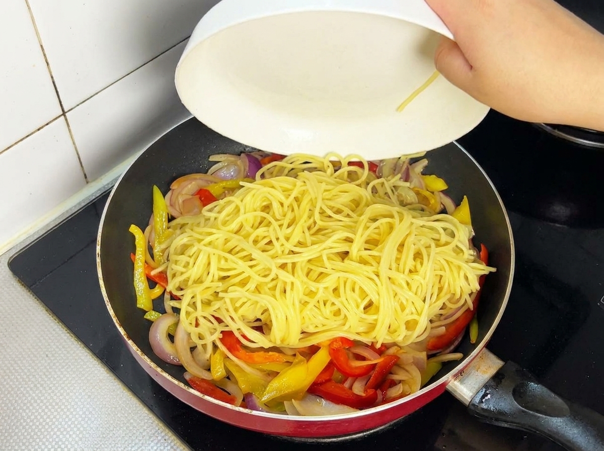 Fettine di manzo cotte aggiunte in padella con spaghetti e verdure.