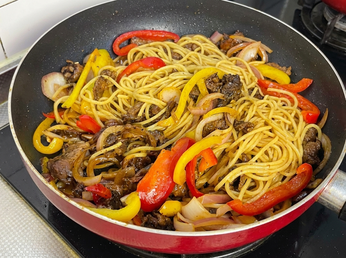 Spaghetti, manzo e peperoni ben conditi e lucidi in padella.