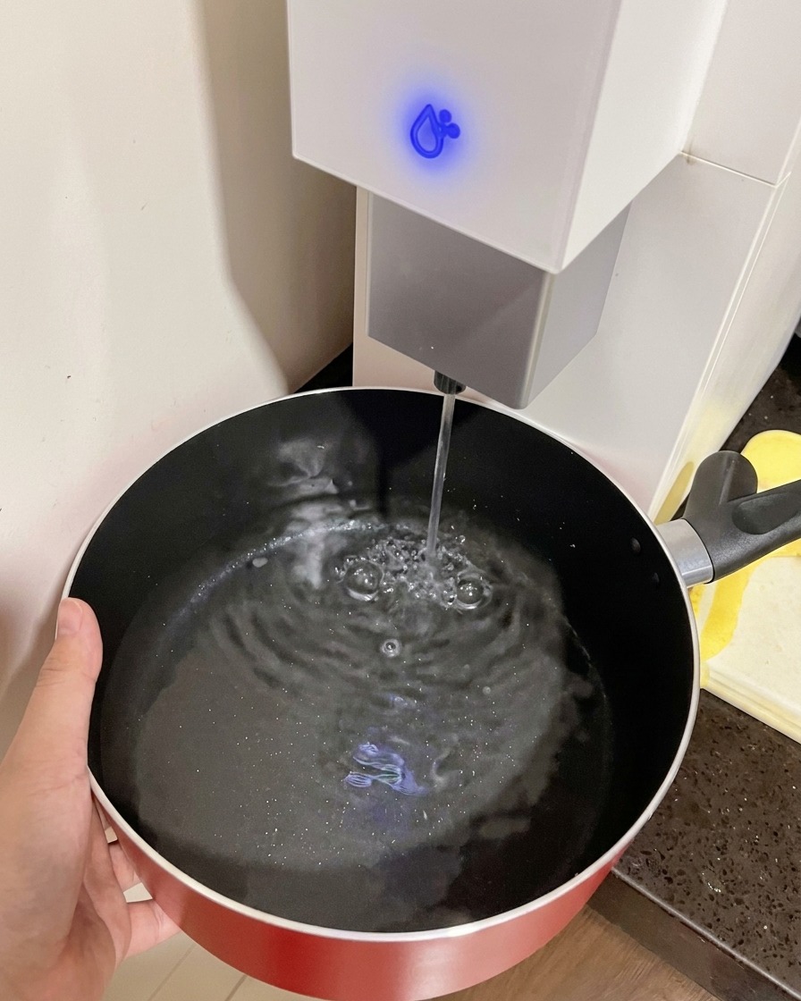 Una mano tiene una pentola rossa mentre viene riempita dacqua dal dispenser.