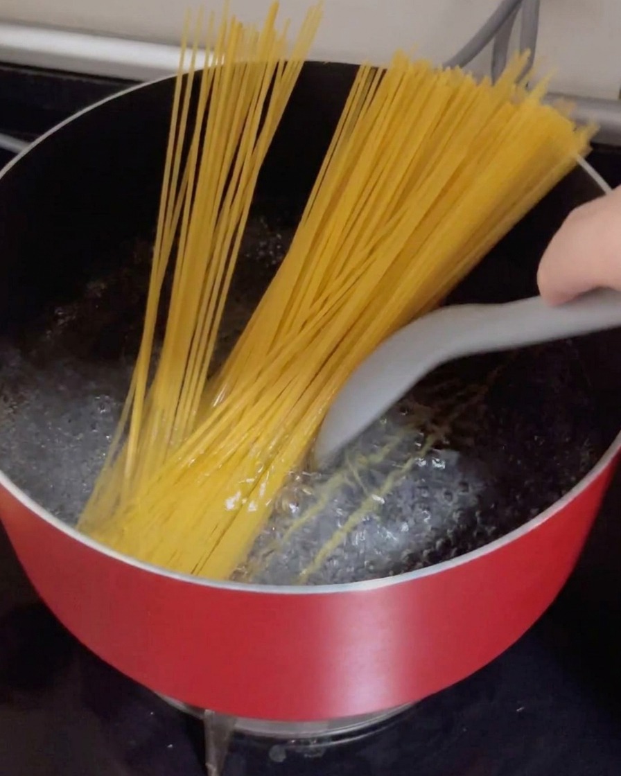 Spaghetti secchi che vengono immersi in una pentola rossa con acqua bollente.