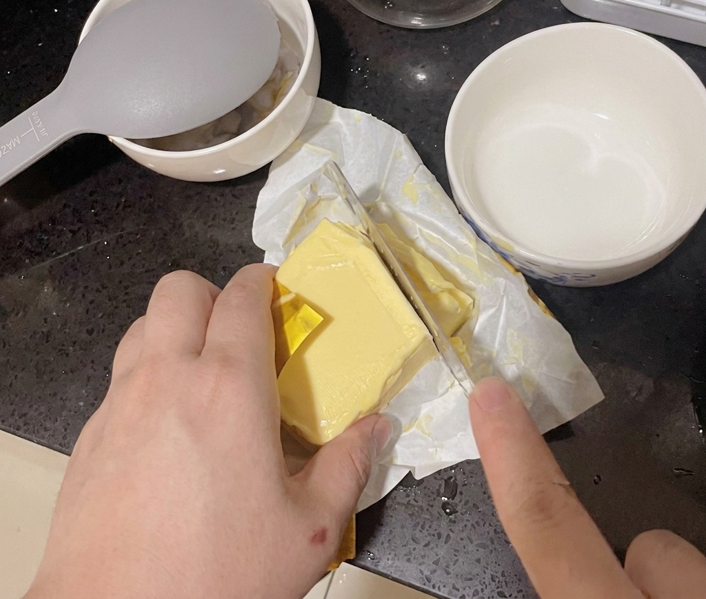 Una persona che taglia una fetta da un panetto di burro usando un coltello da cucina.