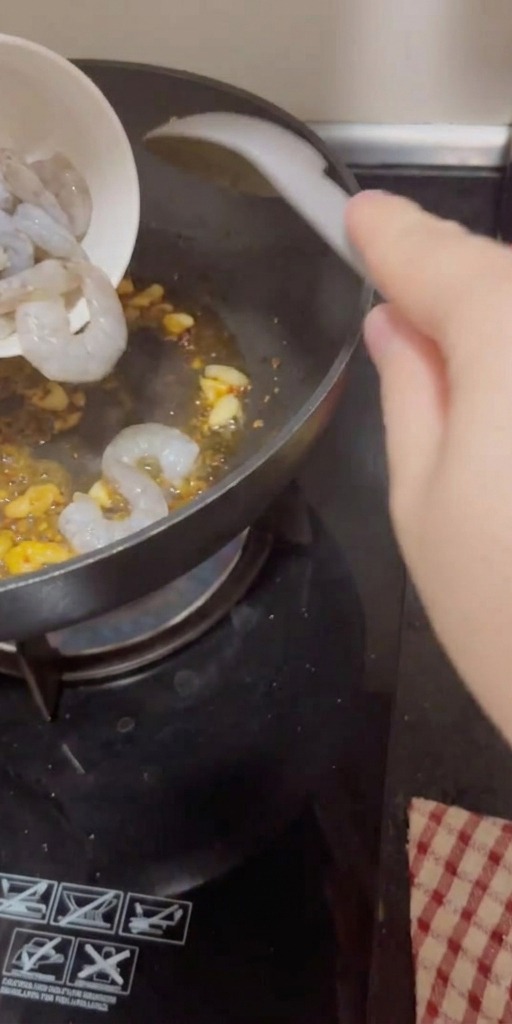 Gamberi crudi versati in una padella calda con aglio e peperoncino sfrigolanti.