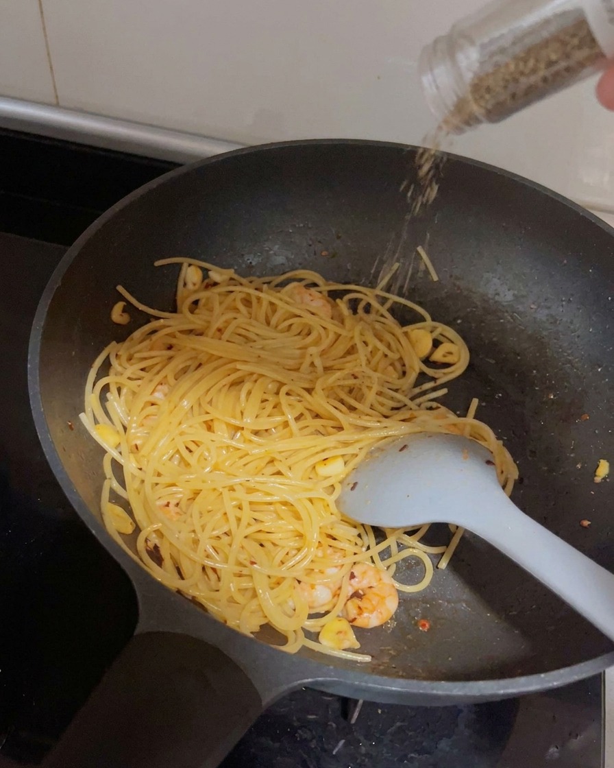 Un macinapepe che dispensa pepe nero fresco sopra la pasta e i gamberi in padella.