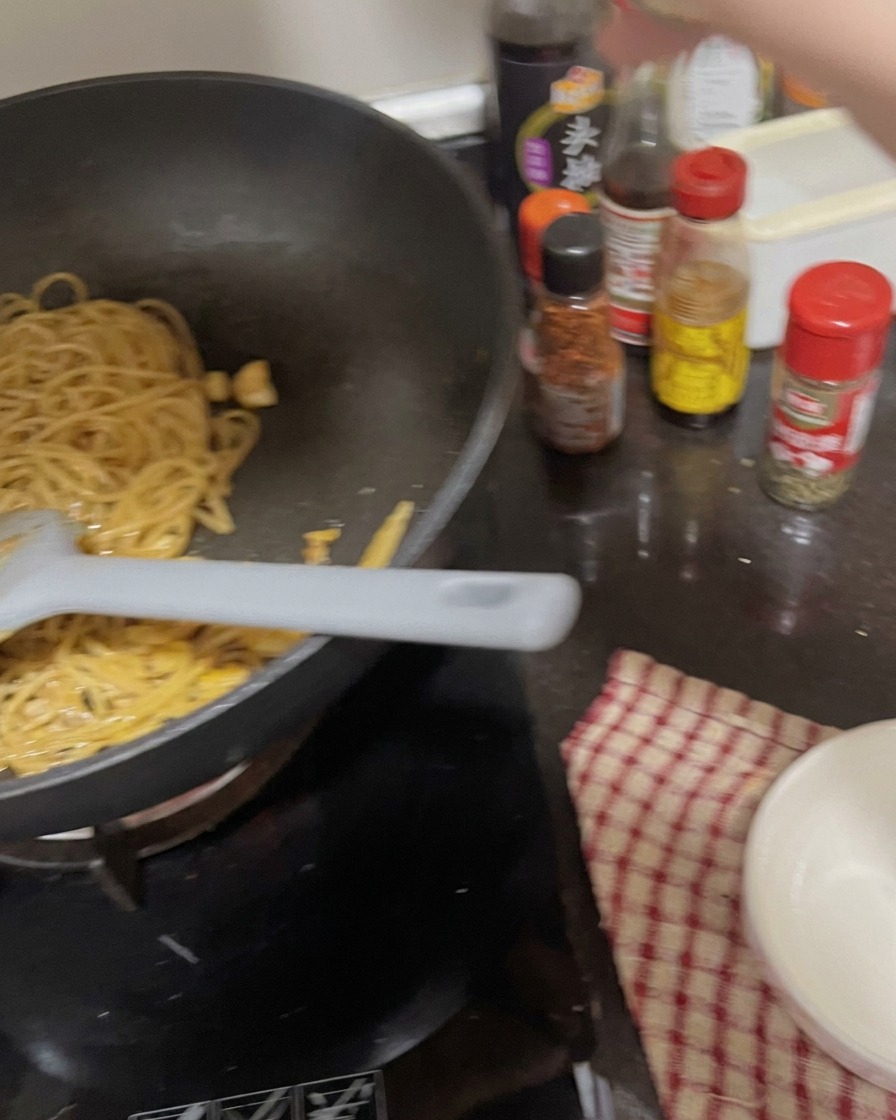 Una mano che spolvera aglio in polvere e prezzemolo sopra gli spaghetti saltati.