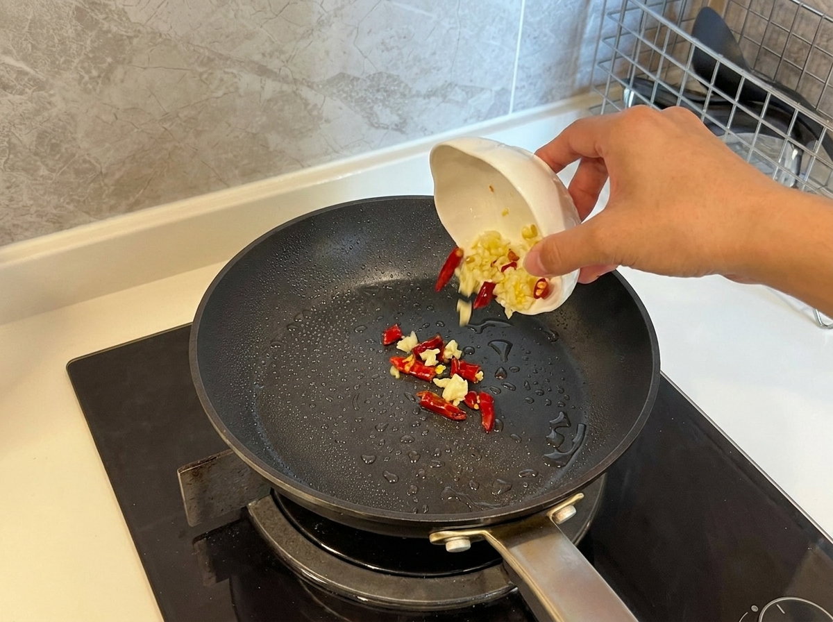 Aglio a fette e peperoncini rossi secchi versati da una ciotolina in una padella calda con olio.